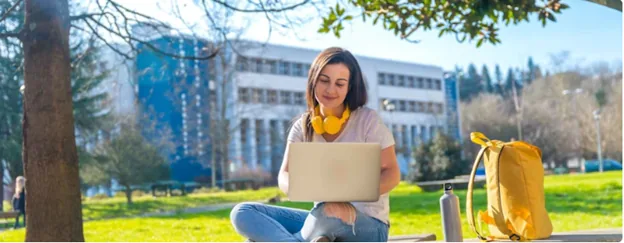 Student studying on a laptop on a university campus lawn